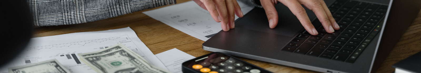 Hands reviewing papers with their laptop and phone of a desk